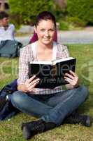 Serious female student reading a book sitting on grass