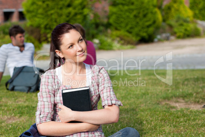 Thoughtful female student reading a book sitting on grass