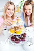 Positive young women eating cakes in the kitchen