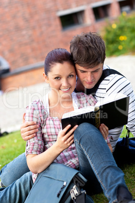 Young couple of students reading a book sitting on grass