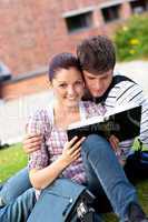 Young couple of students reading a book sitting on grass