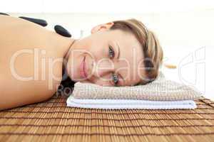 Portrait of a joyful woman lying on a massage table  with hot st