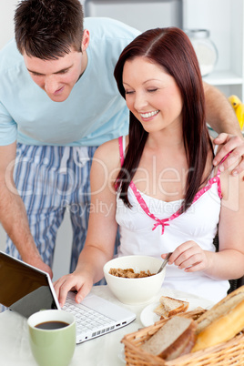 Bright couple using a laptop while breakfast at home