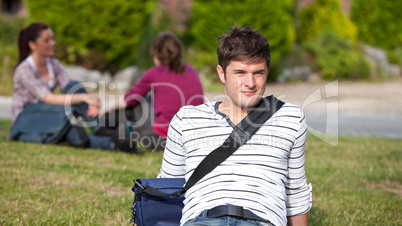 Positive male student lying on the grass with his schoolbag