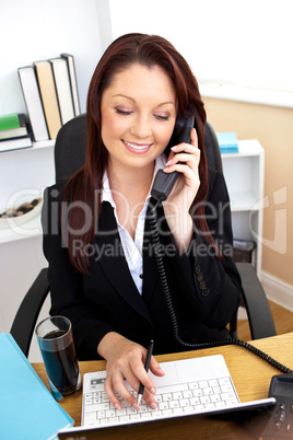 Concentrated businesswoman talking on phone and using her laptop