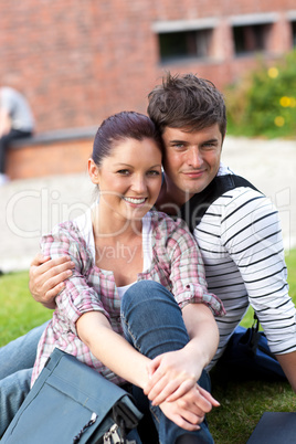 Beautiful couple of students sitting on grass and smiling at the