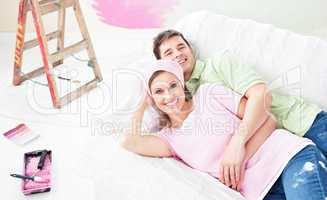 Positive couple lying on a sofa after painting a room