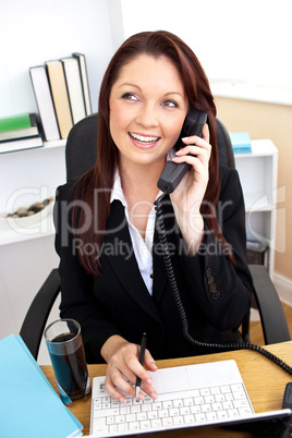 Assertive businesswoman talking on phone and using her laptop at
