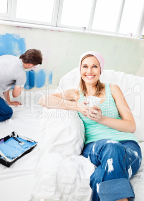 Smiling woman relaxing on a sofa while boyfriend painting the ro