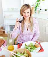 Bright young woman drinking wine and eating a salad in the kitch