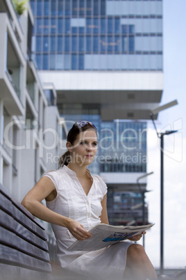 Business female reading paper on a bench