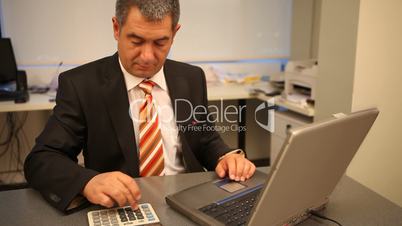 Businessman using laptop in office, calculating