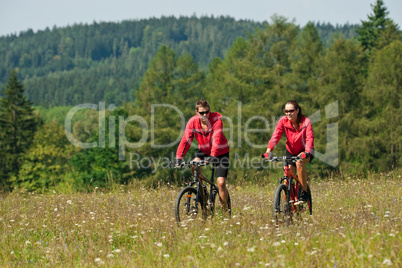 Young couple riding mountain bike in spring meadow