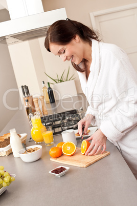 Young woman in bathrobe cutting orange in kitchen