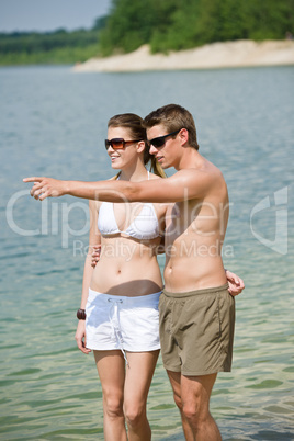 Smiling couple enjoy sun at seashore standing in water