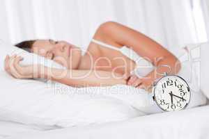 Young woman sleeping in white bed with alarm clock