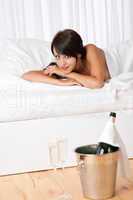 Naked woman lying in white bed with champagne