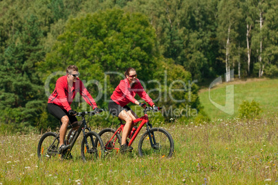 Young couple riding mountain bike in spring meadow