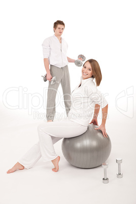 Young couple with weights and fitness ball on white