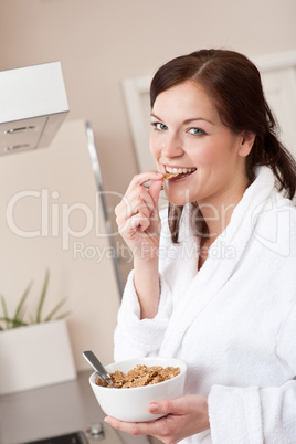 Happy woman eating cereals for breakfast in kitchen