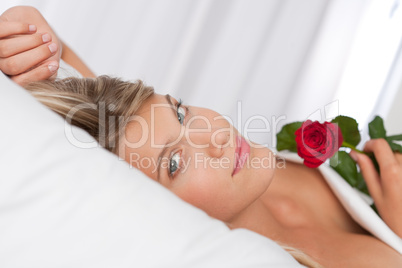 White lounge - Beautiful woman lying in bed holding red rose