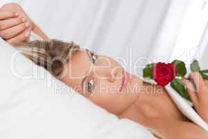 White lounge - Beautiful woman lying in bed holding red rose