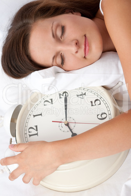 Young woman sleeping in white bed with alarm clock