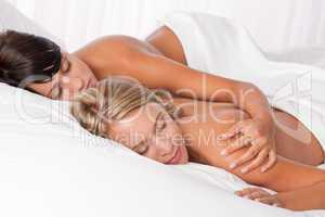 Blond woman and brunette lying down in white bed