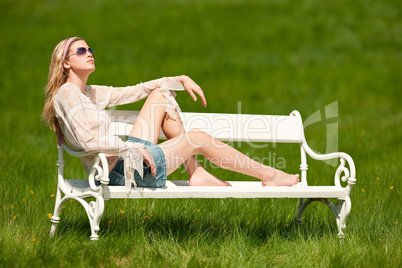 Spring - Young woman relaxing on bench in meadow