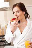 Woman in bathrobe eating toast for breakfast in kitchen