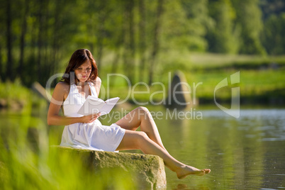 Happy romantic woman sitting by lake with book