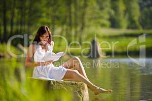 Happy romantic woman sitting by lake with book