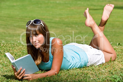 Smiling woman lying down on grass with book