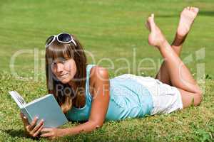 Smiling woman lying down on grass with book