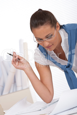 Female architect watching plans and writing notes