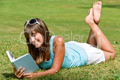 Smiling young woman lying down on grass with book