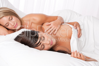 Blond woman and brunette sleeping in white bed