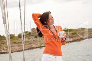 Young woman standing on sailing boat with cup of coffee