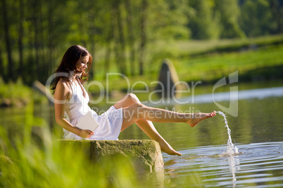 Happy romantic woman sitting by lake splashing water