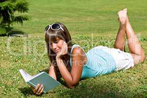 Smiling young woman lying down on grass with book