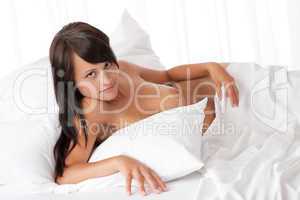 Smiling woman lying naked in white bed