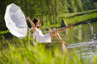 Happy romantic woman sitting by lake splashing water