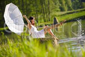 Happy romantic woman sitting by lake splashing water