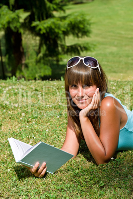 Smiling young woman lying down on grass with book