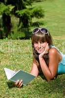 Smiling young woman lying down on grass with book