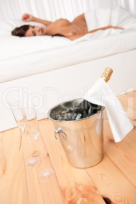 Bottle of champagne in ice bucket, naked woman in background