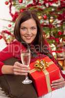 Smiling woman with Christmas present and glass of champagne