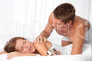 Young man waking up woman in white bed