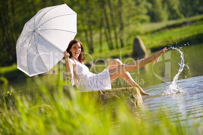 Happy romantic woman sitting by lake splashing water