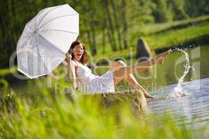 Happy romantic woman sitting by lake splashing water